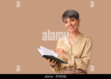 Smiling mature woman with short gray hair holding an open book, education and learning concept, isolated on a brown background Stock Photo