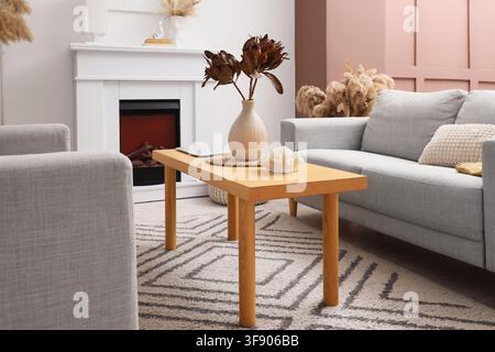 Modern living room interior with light gray sofa, wooden coffee table, and decorative fireplace, cozy home design Stock Photo