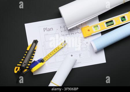 Architectural blueprints and construction tools including a tape measure, level, and utility knife on a dark background Stock Photo