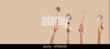Hands holding kitchen utensils including a spaghetti server, two strainers, and a whisk on a beige background with copy space Stock Photo