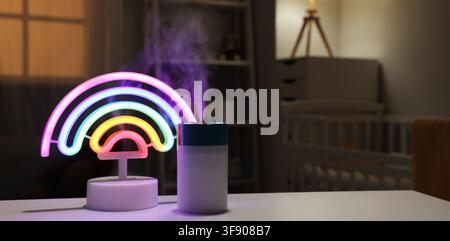 Colorful rainbow neon light and humidifier emitting mist in a cozy baby nursery at night, a humidifier next to the light emits a gentle mist, adding m Stock Photo