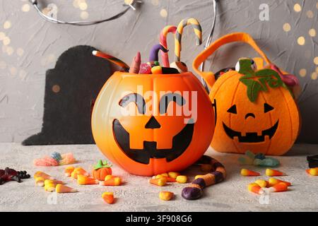 Orange plastic jack-o'-lantern bucket filled with assorted halloween candy and treats on a gray background, a felt pumpkin bag and scattered candies a Stock Photo