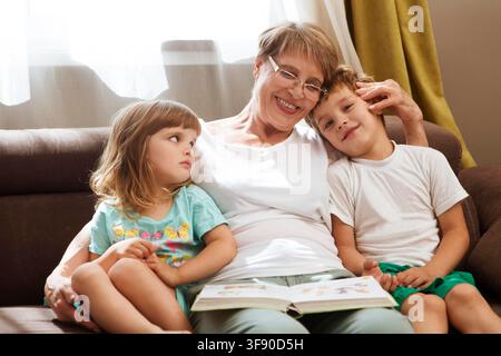 Grandmother with two child grandsons having a great time and reading a book at home. Family Reading Leisure Stock Photo