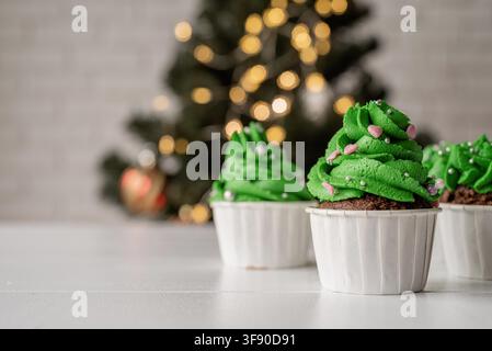 Merry christmas and happy new year. Green Christmas tree shaped cupcakes, surrounded with festive decorations and lights on the background Stock Photo