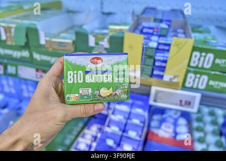 Milbona organic butter is held in one hand in front of a shelf with other butter packs, refrigerated rack, buy product, hold in hand, select, organic Stock Photo