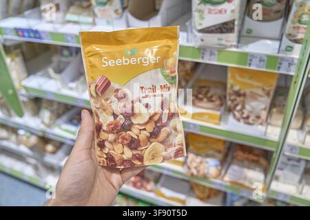 A trail mix with nuts and dried fruit mixed by Seeberger is held by one hand in the supermarket, buy product, pack, bag, plastic bag, Seeberger brand Stock Photo