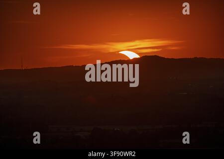 The sun will sink on the horizon during the partial solar eclipse on 12/08/2026, leaving behind an orange sky. The view shows mountains and a clear ev Stock Photo