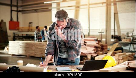Carpenter, phone call and man in workshop for writing notes, production schedule and planning. Construction, contractor and person on cellphone for Stock Photo