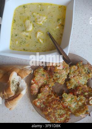 Traditional ukrainian dumpling soup with sour cream paired with fried zucchini fritters and sliced garlic bread stock photo Stock Photo