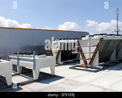 Large industrial cooling and ventilation systems are mounted on the roof of a modern building, with a telecommunications tower visible in the distance Stock Photo