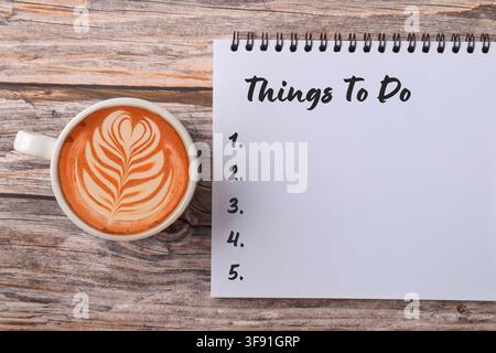 Notebook displaying a Things To Do checklist beside a cup of coffee on a wooden desk, symbolizing task management, productivity, organization, plannin Stock Photo