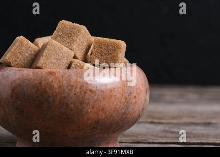 Close up image unrefined brown sugar cubes overflowing from marble bowl on wooden wood Stock Photo