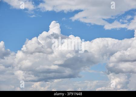 Bright blue sky filled with fluffy white and grey cumulus clouds background on vibrant sunny daylight Stock Photo