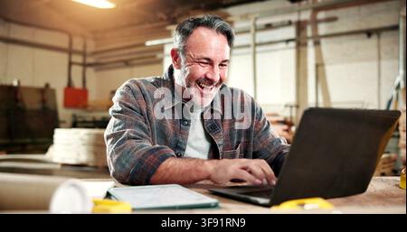 Smile, carpenter and laptop with man in warehouse for construction plan, research and design software. Furniture manufacturing, online project and Stock Photo