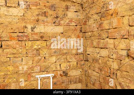 Close-up view of a weathered brick wall featuring a geometric pattern made by thin wires attached to metal fasteners. The bricks display a mix of yell Stock Photo