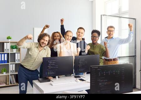 Happy diverse developers team cheering in office after coding project success Stock Photo