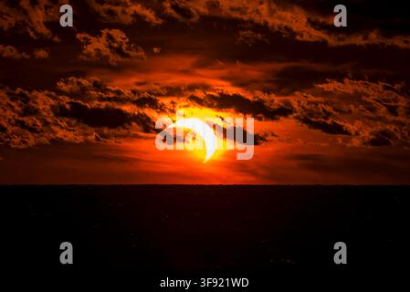 Solar eclipse partially covering the sun during sunset time with dark clouds. Stock Photo