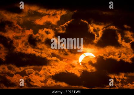Solar eclipse partially covering the sun during sunset with dark clouds. Stock Photo