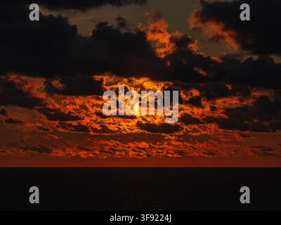 Solar eclipse partially covering the sun during sunset over sea water. Stock Photo