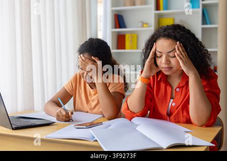 Stressed Black mother and daughter sitting at desk with books and notebooks Stock Photo