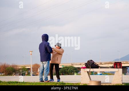 New Taipei City, Taiwan - Feb 19, 2026: Weekend riverside park scene of a senior couple holding hands and dancing together at dusk Stock Photo
