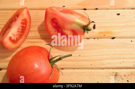 Fresh red tomatoes, including sliced pieces, arranged on a warm wooden surface in a bright overhead food composition. Stock Photo