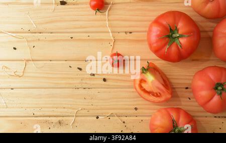 A minimalist overhead composition of ripe tomatoes on pale wooden planks, featuring a sliced tomato, small cherry tomato, scattered soil, and generous Stock Photo