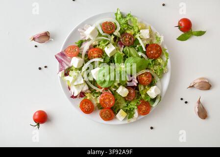 A fresh mixed salad combines leafy greens, tomatoes, feta cubes, onion and basil on a white plate, creating a colorful, light Mediterranean meal. Stock Photo