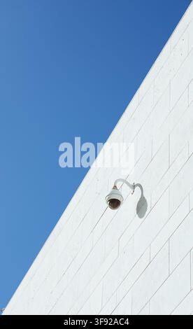 Minimalist security camera on a white wall against blue sky Stock Photo