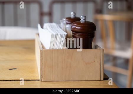 The rustic condiment organizer with white napkins and brown wooden spice mill rests on a table, providing essential service items for guests in a warm Stock Photo