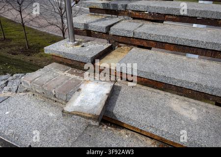 Weathered outdoor stone steps showing significant structural damage and orange rust, representing urban decay, safety hazards, and a requirement for p Stock Photo