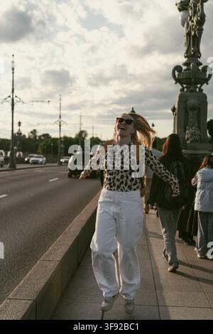 Happy young woman laughs while jumping on a sidewalk Stock Photo
