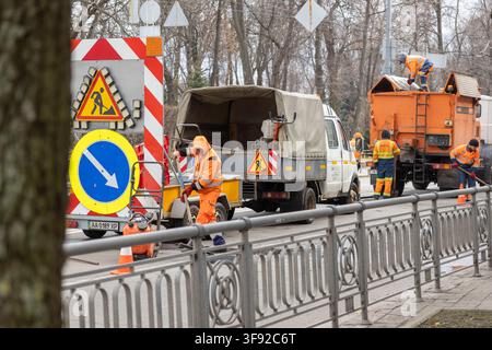 Kyiv, Ukraine - March 22, 2026: Dedicated workers in reflective uniforms patch potholes on a busy city road using heavy equipment to ensure safe trans Stock Photo
