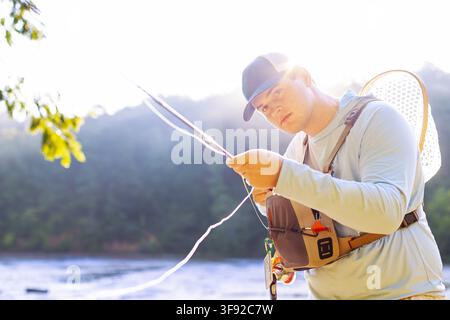 Focused young man fly fishing by a sunny river Stock Photo