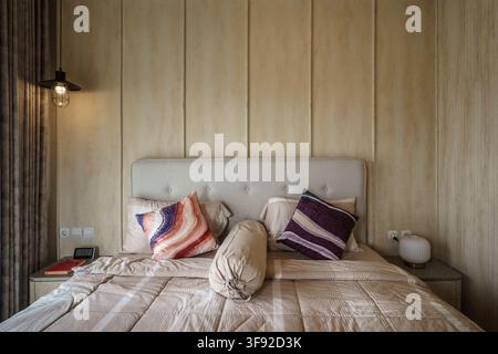 Neatly arranged comfortable bed in a warm cozy bedroom featuring neutral plaid bedding, colorful patterned throw pillows, and a traditional bolster Stock Photo