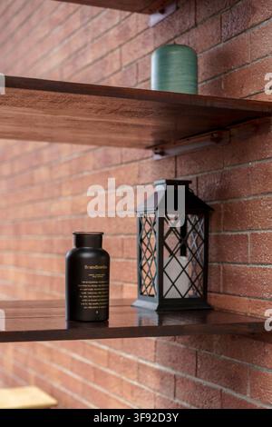 Close up of a rustic interior featuring a dark wooden floating shelf mounted on an exposed red brick wall. On the wooden shelf sits a black candle Stock Photo