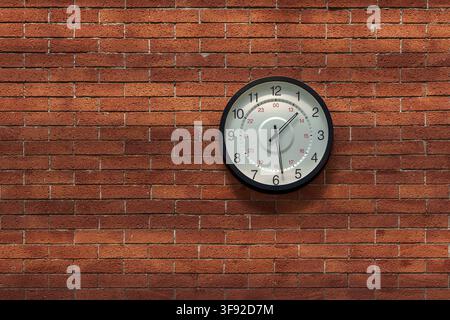 A classic round analog wall clock with a black rim and white face mounted centrally on a textured red brick wall background. Stock Photo