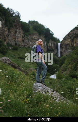 Smiling female hiker enjoys view with waterfall Stock Photo
