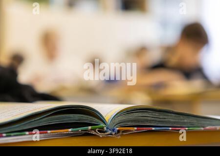 A close up view of an open book on a classroom desk during a lesson, with blurred children studying in the background, representing elementary educati Stock Photo