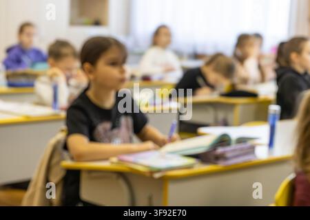 Children sitting at wooden desks in a bright primary school classroom, working diligently on their lessons to reflect the atmosphere of concentration Stock Photo
