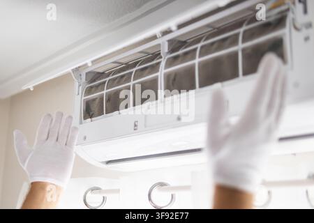 Technician wearing white gloves inspecting dirty air conditioner filters, performing cleaning and maintenance to improve indoor air quality and coolin Stock Photo