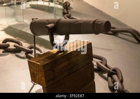 A close view shows an antique iron restraint device mounted on a wooden stand with large metal chains in a museum display. Stock Photo