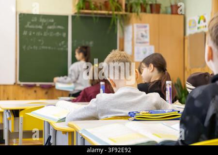 Primary school students focused at their desks in a classroom, with one pupil performing a task at the blackboard, capturing the essence of academic g Stock Photo