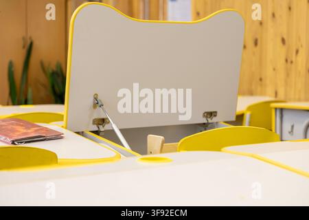 Empty primary school classroom featuring modern yellow desks with open lids for storage, creating an organized and welcoming learning environment for Stock Photo
