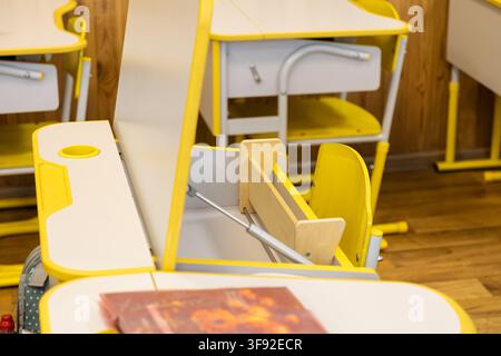 Empty primary school desks featuring adjustable surfaces and storage compartments inside a vibrant classroom setting, designed to encourage productive Stock Photo