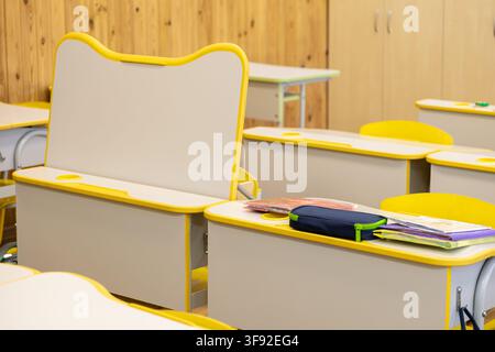 Empty primary school classroom featuring modern yellow desks and chairs, designed for an engaging educational space where students develop skills in a Stock Photo