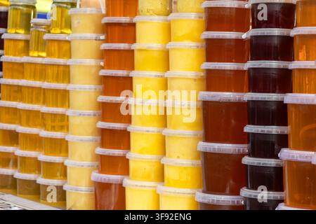 Assortment of translucent plastic containers packed with golden and dark raw honey stacked neatly, conveying a vibrant market setting focused on fresh Stock Photo