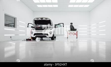 white SUV in modern auto detailing studio workshop. Wide shot of a white car with hood & doors open in modern brightly lit white auto detailing center Stock Photo