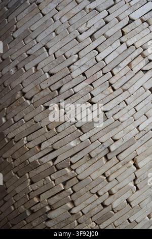 Vertical detailed close-up shot of small off-white marble stone strips arranged diagonally to form a unique textured surface. The stacked stone. Stock Photo