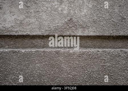 Detailed shot of a coarse concrete wall surface featuring a prominent horizontal indented groove line across the middle. Stock Photo